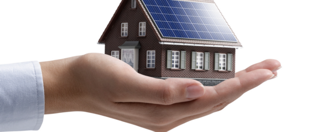 Hand holding a model house with solar panels, symbolizing District Energy's commitment to residential solar energy solutions and sustainability.